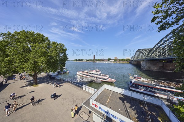 Rhine river, pedestrian and railway bridge Hohenzollern bridge, arched bridge, general architecture, waterfront, boat launch, gangway, wharf, excursion boats, Cologne-Düsseldorfer Deutsche Rheinschiffahrt GmbH, footpath, pedestrians and cyclists as secondary motif, trees, bird's-eye view, blue sky, cirrus clouds, Trankgassenwerft, Cologne, district-free city, North Rhine-Westphalia, Germany