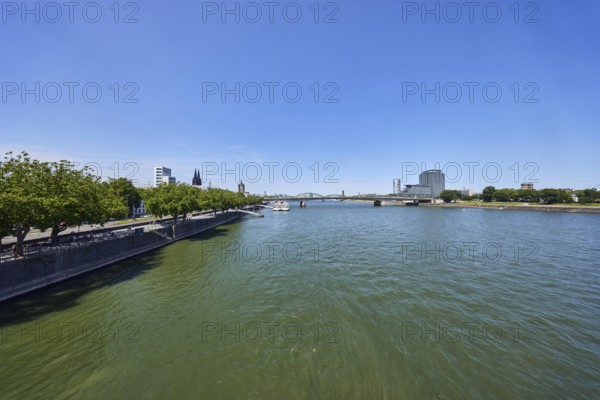 Rhine river, general architecture, high-rise MaxCologne, riverbank, church towers, Cologne Cathedral, quay wall, waterfront, bridge, trees, water surface with small waves, blue sky, cloudless, Leystapelwerft, Deutz bridge, Deutz shipyard, Cologne, district-free city, North Rhine-Westphalia, Germany