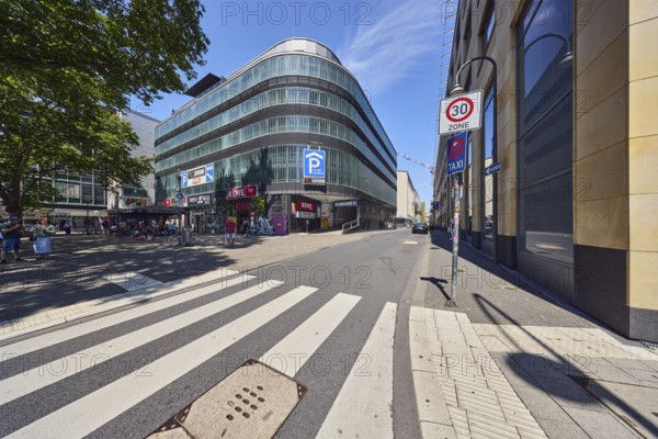 Parking garage, HECON Car Parking GmbH, modern architecture, commercial building, pedestrian area, street, pedestrian crossing, zebra crossing, zone 30 sign, Saturn Elektromarkt, Lebensmittel REWE Markt GmbH, pedestrians as accessories, trees, blue sky, cirrus clouds, Große Sandkaul, Cologne, district-free city, North Rhine-Westphalia, Germany
