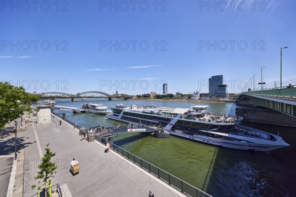 Rhine river, waterfront, sightseeing boats, general architecture, high-rise buildings, modern architecture, lantern, pedestrian and railway bridge Hohenzollern Bridge, trees, pedestrians and visitors to an excursion ship as a secondary motif, elevated perspective, blue sky, cirrus clouds, Deutz bridge, Leystapelwerft, Cologne, district-free city, North Rhine-Westphalia, Germany