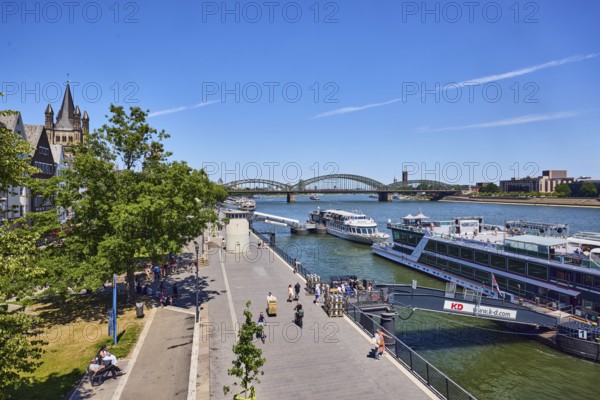 Rhine river, waterfront, sightseeing boats, general architecture, skyscrapers, modern architecture, church tower of Gross St. Martin, pedestrian and railway bridge Hohenzollern Bridge, trees, cyclists, pedestrians and visitors to a tour ship as a secondary motif, elevated perspective, blue sky, cirrus clouds, Deutz bridge, Leystapelwerft, Cologne, district-free city, North Rhine-Westphalia, Germany