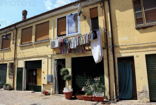 The laundry hangs to dry on a line outside the window, next to it an air conditioner, typical scene, street scene at lunchtime, from the small town of Mesola in the Po Delta, province of Ferrara, Emilia-Romagna, Italy/The laundry hangs to dry on a line in front of the window, next to it an air conditioner, typical scene from the small town of Mesola in the Po Delta, province of Ferrara, Italy
