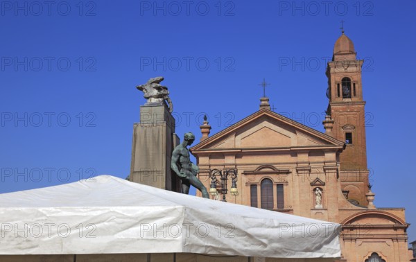 Monument with a statue in Piazza Unita and the Santo Stefano Collegiate Church in the city of Novellara, Emilia-Romagna, Italy