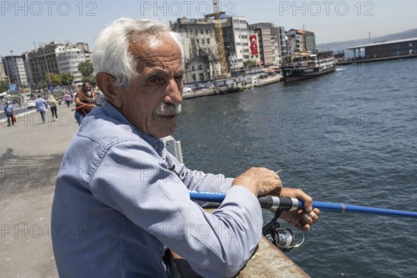 Istanbul, Turkey. June 23rd 2025. An old Turkish man fishing on the Galata Bridge near Karikoy ferry port on the European side of Istanbul, Turkey