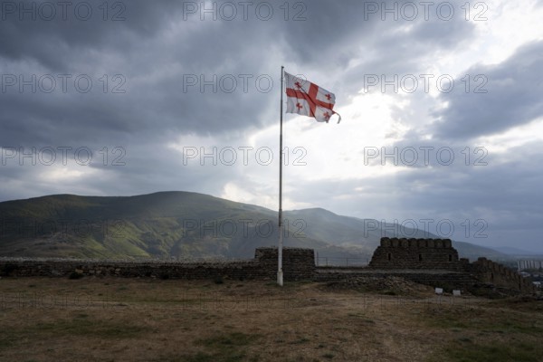 Dramatic heavy clouds and the Georgian flag over the mountain landscape surrounding Gori city birthplace of Soviet politician Joseph Stalin, Georgia