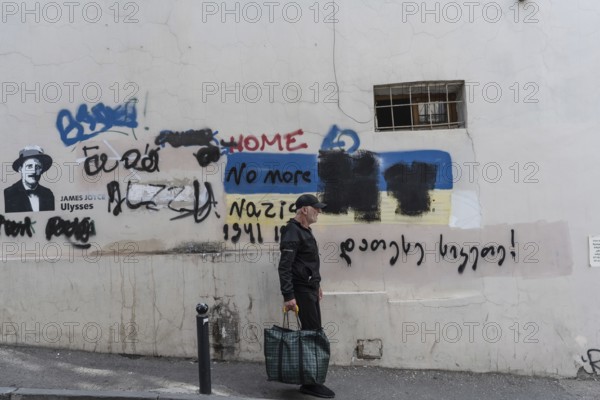 Tbilisi, Georgia. July 7th 2025. An elderly local man walks past a wall of graffiti in a side street of the Old Town in Tbilisi, Georgia