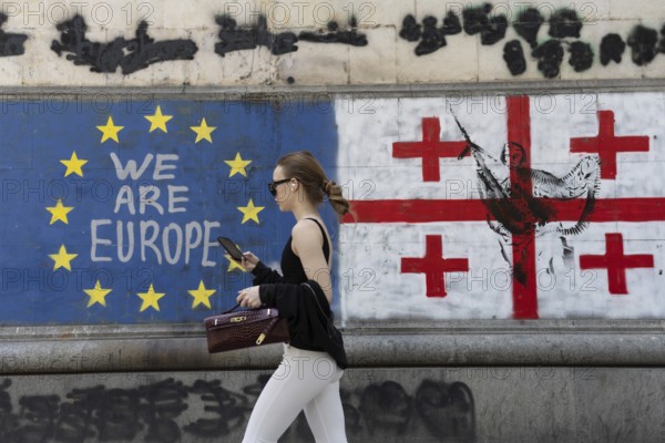 Tbilisi, Georgia. July 7th 2025. A woman walks past the flags of Georgia and the European Union along Shota Rustaveli Avenue near to Freedom Square, in central Tbilisi, Georgia