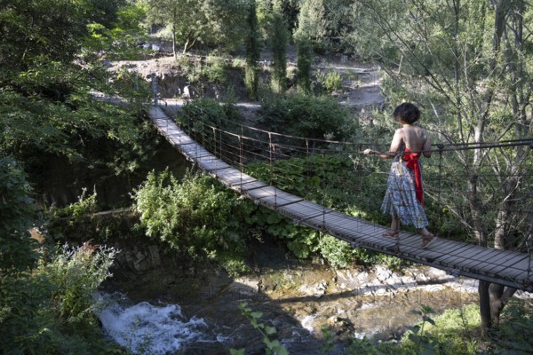 Tbilisi, Georgia. July 13th 2025. A foreign tourist crosses a wooden rope bridge inside the National Botanical Garden of Georgia in the Tsavkisis-Tskali Gorge, Tbilisi
