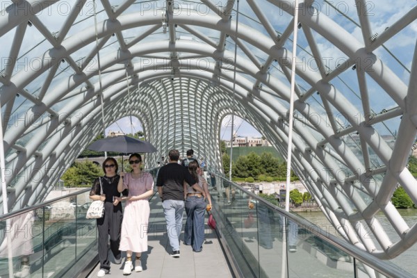 Tbilisi, Georgia. July 7th 2025. Tourists cross The Bridge of Peace over the Kura River in the Georgian capital, Tbilisi, Georgia