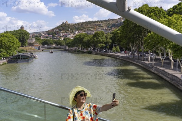 Tbilisi, Georgia. July 7th 2025. An Asian tourist poses for a photograph on the Bridge of Peace over the Kura River in the Georgian capital, Tbilisi, Georgia