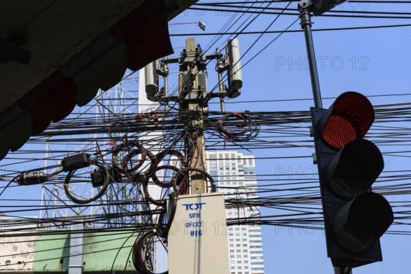A red traffic light with a tangled mess of cables and wires with mobile communication mast, Bangkok city centre, Thailand. Asia