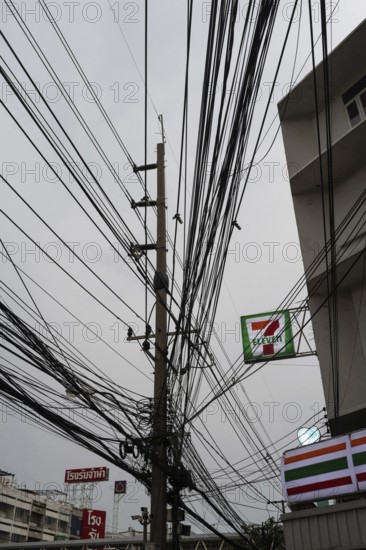 Bangkok, Thailand. March 4th 2025. A tangled mess of cables and wires used for phone and internet connections hanging from a pole in the street outside a 7 Eleven store in central Bangkok, Thailand