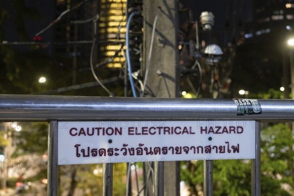 Bangkok, Thailand. March 4th 2025. A Caution Electrical Hazard sign near an electricity pylon with exposed wiring in central Bangkok, Thailand, Asia