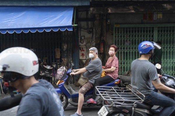 Bangkok, Thailand. March 18th 2025. An elderly couple wearing masks on a motor scooter in the busy streets of the Talat Noi neighbourhood of Bangkok, Thailand, Asia