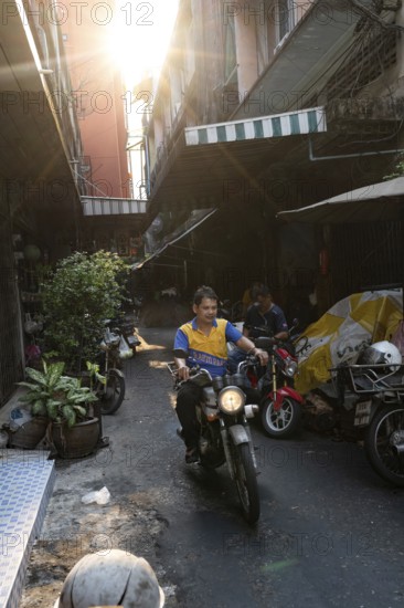 Bangkok, Thailand. March 18th 2025. A motorcycle mechanic rides through the narrow streets of Talat Noi, Bangkok, Thailand, Asia