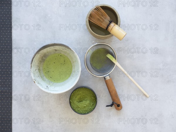 Matcha powdered tea and whisked beverage with bamboo tools on a grey backdrop