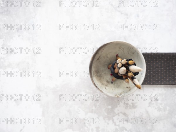 Paint brushes with bamboo handles are bundled together in a ceramic bowl, resting on a white table next to a patterned cloth