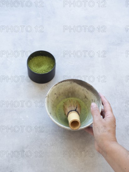 Hand holding a traditional japanese chawan with matcha and bamboo whisk