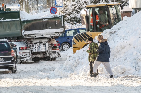 Two children playing among cars and loaders clearing snow on streets in Ystad, Skåne County, Sweden, Scandinavia