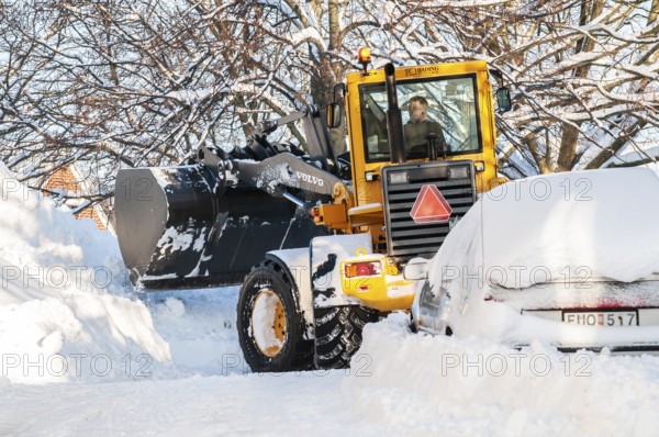 Loader clearing snow among snow-covered cars on streets in Ystad, Skåne County, Sweden, Scandinavia
