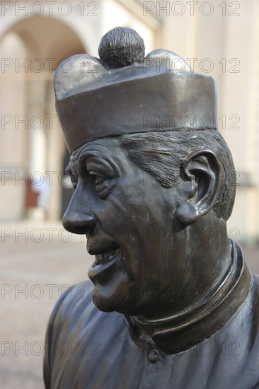 Italy, in the village of Brescello, statue of Don Camillo, portrayed by actor Fernand Joseph Desire Contandin, known as Fernandel, in front of the church of Santa Maria Nacente e San Genesio, Emilia Romagna, Italy
