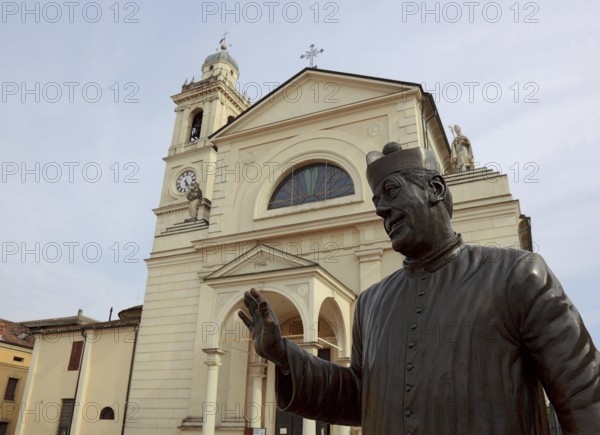 Italy, in the village of Brescello, statue of Don Camillo, portrayed by actor Fernand Joseph Desire Contandin, known as Fernandel, in front of the church of Santa Maria Nacente e San Genesio, Emilia Romagna, Italy