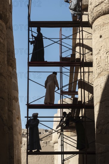 Luxor, Egypt. December 12th 2022 Silhouetted local Egyptian workers cleaning and restoring the ancient columns of Karnak Temple near the River Nile, Luxor, Upper Egypt