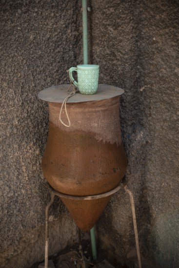 A local clay public clean water drinking fountain with plastic mug, along the Nile River in Upper Egypt near the city of Aswan, Egypt