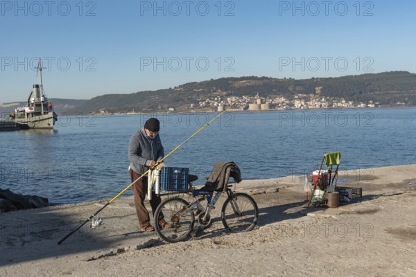 Canakkale, Turkey. February 18th 2022 A Turkish fisherman on the pier at Canakkale, with the Dardanelles Straight, Gallipoli Peninsula and Kilitbaher in the background