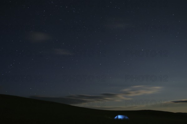 Illuminated tent stands alone in Mongolian steppe under starry sky at night, Nömrög National Park, Dzavhan, Mongolia