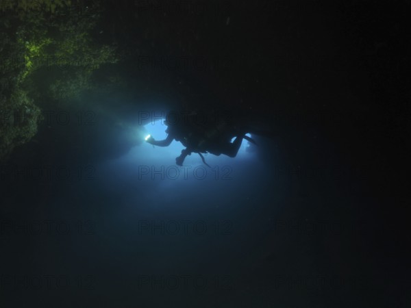 Diver, cave diver with lamp in dark underwater cave explores the surrounding area. Fraskeric dive site, Stoja, Pula, Croatia, Mediterranean