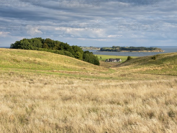 Hilly landscape in the Zicker Mountains under dramatic stormy clouds, including Zicker Alps, view over dry meadows to a fishing farm and the Klein Zicker peninsula, Mönchgut nature reserve, Gross Zicker, Mönchgut peninsula, Rügen island, Mecklenburg-Western Pomerania, Germany