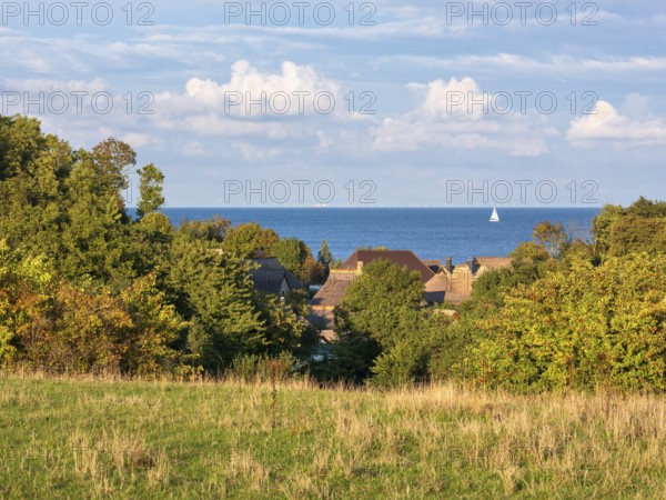 View over the thatched roofs of the fishing village of Vitt to the Baltic Sea, a sailboat on the water, Cape Arkona, Rügen island, Mecklenburg-Western Pomerania, Germany