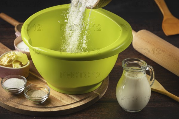 Flour falls into a green bowl surrounded by baking ingredients