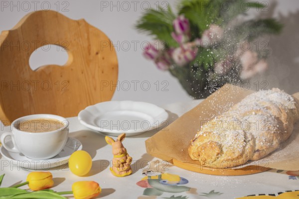 Yeast braid is sprinkled with sugar, breakfast table with coffee and decoration for Easter