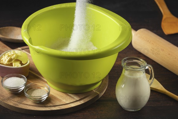 Sugar falls into a green bowl surrounded by baking ingredients
