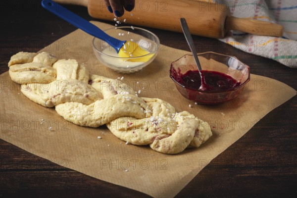 Hail sugar falls on raw yeast braid next to jam and a bowl of milk