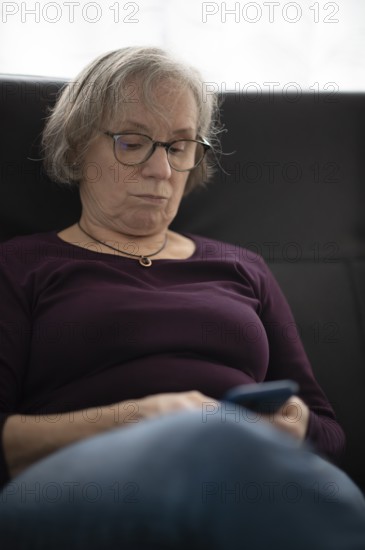 Elderly woman with glasses, gray hair, sitting on sofa and using smartphone, cell phone, Stuttgart, Baden-Württemberg, Germany