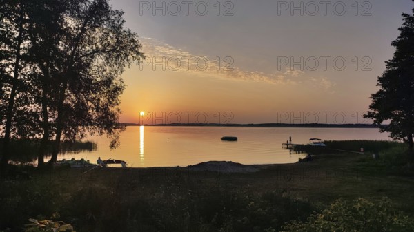 A quiet, atmospheric sunset on a lake with trees and a boat dock, bicycle tour through Masuria, Poland