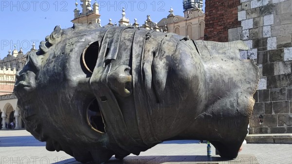 Large sculpture of a head, Eros Bendato, lying in a busy square, Krakow, Poland