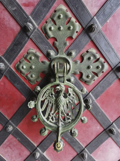Decorative door knocker on red background decorated with coat of arms and metal ornaments, Poland