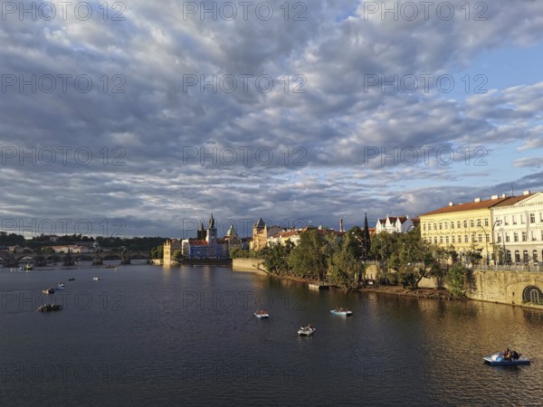 Prague in the evening sun. Vltava surrounded by illuminated historic buildings, small boats floating on calm water, Prague, Czech Republic