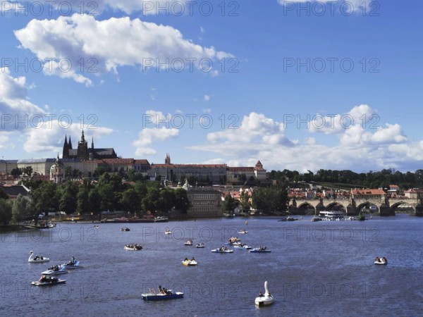 Summer hustle and bustle on the Vltava in Prague with Charles Bridge and Hradcany in the background, picturesque river landscape with boats, castle towers and an old bridge under a blue sky, Prague, Czech Republic