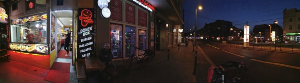 Panorama Lively evening street scene with illuminated snack bar and urban atmosphere, Pankow, Berlin