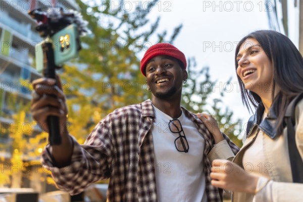 Diverse friends documenting moments with a smartphone on a gimbal stabilizer, recording content for their online audience while smiling outdoors in an urban setting