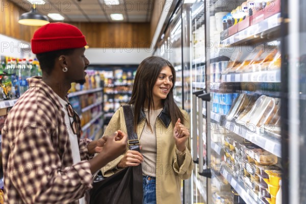 Diverse couple browsing refrigerated display at grocery store, making choices for healthy eating, representing modern lifestyle and consumerism in retail environment