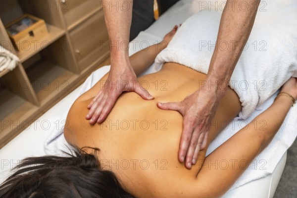 Hands of a professional therapist giving a deeply relaxing and therapeutic back massage to a woman lying on a table, promoting wellness and stress relief in a serene spa setting