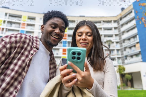 Young diverse friends smiling and sharing content on a smartphone outdoors, enjoying social media, digital connection and casual conversation in a modern urban setting