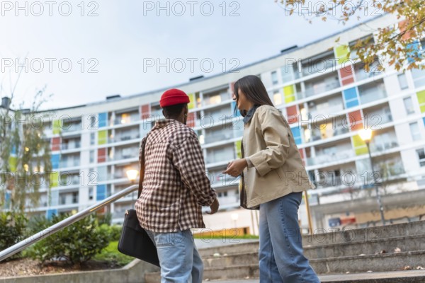 Diverse young adults walking and talking down outdoor steps in a modern urban neighborhood with a colorful building backdrop, sharing conversation and casual connection