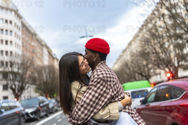 Happy diverse couple embracing outdoors, a man kissing his smiling girlfriend's forehead on a city street, showing affection and a strong relationship
